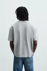 Camiseta gris con cuello redondo y manga corta. Presenta estampados, bordados y parches frontales combinados a contraste. Tiene un efecto lavado.