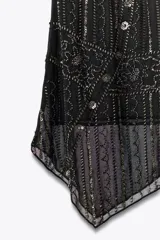 Falda corta negra de tiro medio, con bajo asimétrico. Presenta bordados y aplicaciones de abalorios en tonos plateados y dorados, con un diseño que incluye franjas verticales y motivos florales.