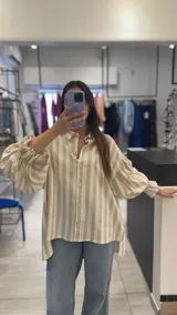 Camisa a rayas verticales color beige y blanco, de corte holgado, con cuello camisero y mangas largas abullonadas con puños elásticos.