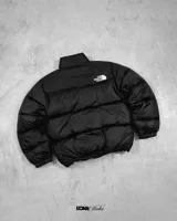 Campera puffer The North Face, color gris y negro, con cierre frontal y cuello alto. Logo de la marca bordado en el pecho.