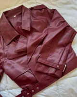 Campera corta de cuero sintético color borgoña, con cuello solapa, corte oversize, cierre cruzado con hebillas y cinturón.