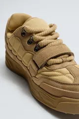 Zapatilla estilo skate de diseño robusto, confeccionada en una combinación de piezas de gamuza y material textil acolchado. Presenta un sistema de cierre con cordones gruesos y una tira de velcro en el empeine, junto con una suela de plataforma con relieve irregular.