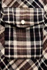 Vestido largo tipo camisero con estampado de cuadros en tonos marrón, negro y blanco. Tiene cuello solapa, mangas largas con puños abotonados, dos bolsillos de parche con solapa en el pecho y cierre frontal con botones a presión.