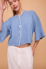 Saco tejido a máquina en lino y algodón color celeste, con silueta en línea A, mangas anchas, escote redondo con bordado en la delantera y botones de nácar. Largo por arriba de la cola.