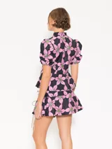 Top con estampado de flores rosas y verdes sobre fondo azul marino, cuello mao con jareta y tiras de gamuza para anudar. Escote en forma de gota, acceso mediante botones forrados en tela base, corte en cintura que le da vuelo a la cadera y mangas abullonadas con elástico en el puño.