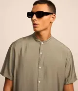 Camisa de manga corta, corte slim, color verde oliva con textura. Presenta cuello padre y cierre frontal de botones.