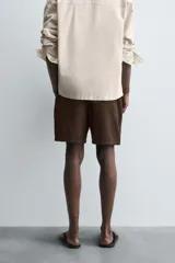 Bermuda de algodón color marrón oscuro, de corte regular fit, con cintura elástica ajustable mediante cordón. Presenta bolsillos laterales y un bolsillo trasero de vivo.