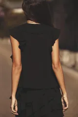 Blusa negra sin mangas con escote en pico y volantes. Cierre frontal con botones y lazo fino con apliques dorados.