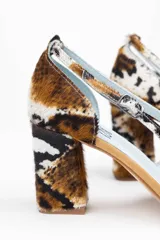 Zapatos de tacón con estampado animal print en tonos marrón, blanco y negro. Tienen punta fina, pulsera con hebilla lateral y tacón ancho. Interior de piel y suela de cuero.