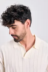 Sweater de tejido de punto color crudo, manga corta, con cuello polo y escote en V. Presenta un diseño acanalado vertical.