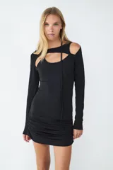 Vestido mini negro de manga larga en tejido elástico, con diseño ceñido al cuerpo y detalles cut-out en la parte superior. Lazada al cuello.