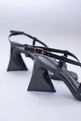 Sandalias de tacón alto color violeta metalizado, con tiras finas cruzadas en el empeine, puntera cuadrada y cierre con hebilla en el tobillo. El tacón es geométrico con forma de triángulo invertido.