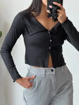 Remera negra de tejido de punto acanalado, con cuello polo, cierre frontal con botones y mangas largas.