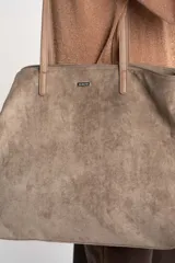 Bolso tipo tote bag grande color camel, confeccionado en cuero vegano con textura de gamuza. Tiene doble asa de hombro y logo de la marca en el frente.