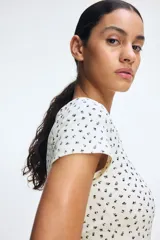 Remera blanca con estampado de flores pequeñas en negro, escote cuadrado y tapeta de botones. Corte entallado y mangas cortas.