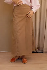 Falda midi color marrón claro, tipo delantal, confeccionada en tela de algodón. Se ajusta a la cintura con tiras.