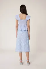 Falda midi de tul celeste bordada con flores y lentejuelas. Tiene forro de tejido tipo cuadros vichy con calados transparentes, cintura elástica y corte recto, ligeramente acampanado en el bajo.