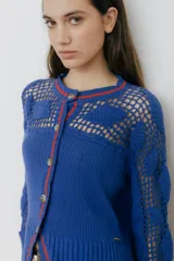 Cárdigan azul con detalles en crochet, mangas con volado y vivos de color rojo en cuello, puños y frente. Tiene botones al frente.