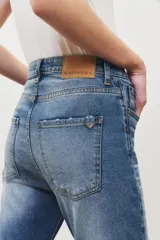 Pantalón jean de tiro medio, corte slim, color azul claro, con rotura en la rodilla y terminación desflecada.