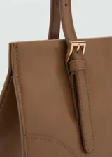 Bolso tipo tote de color crema, con efecto piel, forro interior, asa corta y asa de hombro. Tiene cierre a presión y cierre de cremallera, bolsillo interior y hebillas decorativas.