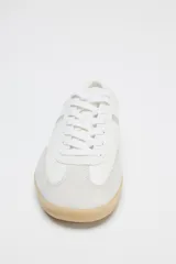 Zapatillas deportivas blancas con detalles plateados y suela color caramelo.