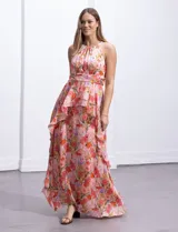 Vestido largo de gasa estampada con flores en tonos naranja, rosa y lila. Tiene escote halter, busto plisado, corte en la cintura con faja plisada y falda con sobrecapa y forro interno a tono.