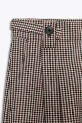 Pantalón de tiro alto con estampado de cuadros en tonos marrón y beige, con bolsillos delanteros y falsos bolsillos traseros. Detalle de trabillas con botones en la cintura. Cierre frontal con cremallera y ganchos metálicos.