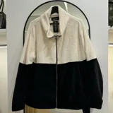 Campera de polar combinada en blanco y negro, con cuello alto y cierre frontal.