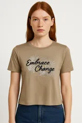 Remera color marrón con estampado frontal con la frase "Embrace Change" en letras negras y plateadas.