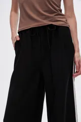 Pantalón negro ancho de viscosa con vivos laterales en blanco, dorado y marrón.