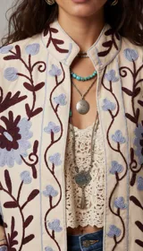 Chaqueta color crema con bordados florales en tonos azul, violeta y marrón. Tiene cuello mao y mangas tres cuartos.