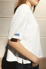 Remera blanca de algodón con cuello redondo y mangas cortas. Presenta un bordado del sol de la bandera uruguaya en el pecho.