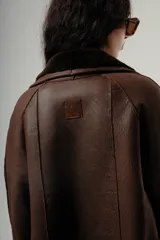 Gamulán de color marrón con interior de corderito al tono, cuello de solapa ancha, cierre frontal con botones y bolsillos laterales con solapa.