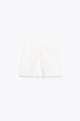 Falda pantalón corta de tiro alto color blanco con detalle de doble fila de botones negros en el frente y cierre lateral con cremallera oculta.