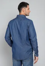 Camisa de jean azul con botones blancos, mangas largas con puños doblados y corte clásico.