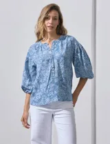 Blusa celeste con estampado floral blanco, escote en V y botones. Mangas 3/4 abullonadas con terminación elastizada.