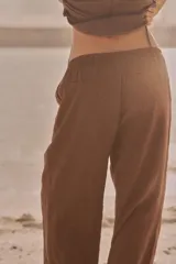 Pantalón marrón de tejido fluido, tiro medio, cintura elástica ajustable con cordones, bolsillos laterales y falsos bolsillos de vivo en la espalda.
