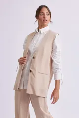 Chaleco largo color beige con solapas, cierre con dos botones y bolsillos delanteros.