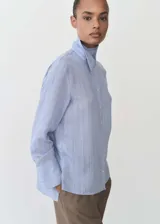 Camisa celeste con rayas verticales finas, de tejido fluido, manga larga abotonada, cuello camisero y corte recto.