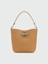 Bolso tipo bucket XS de cuero color crema, con asa corta y correa larga extraíble. Cierre con broche metálico plateado.