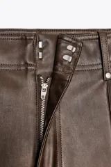 Pantalón marrón de tiro alto con efecto cuero, bolsillos de parche en la parte trasera y costuras marcadas en la parte delantera. Cierre frontal con cremallera y gancho metálico.