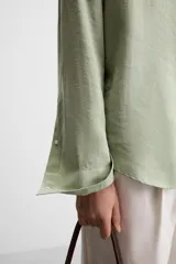 Camisa verde claro de corte relaxed fit confeccionada en tejido con mezcla de modal. Tiene cuello italiano, manga larga con puños abotonados, bolsillo de parche en el pecho y cierre frontal abotonado.