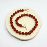 Collar de cuentas de ágata roja de 10mm con separadores de hilo rojo y terminaciones en acero con baño de oro.