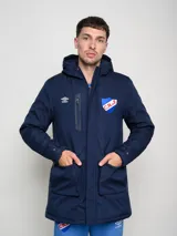 Parka blanca con capucha, cierre frontal con cremallera y botones a presión, cuatro bolsillos frontales con solapa y puños ajustables. Incluye logo de Umbro y escudo del Club Nacional de Football en el pecho.