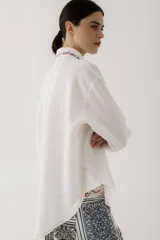 Camisa blanca de lino con bordados de palabras en hilo de colores. Tiene cuello clásico, cierre con botones y bolsillo en el pecho.