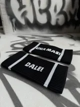 Par de muñequeras deportivas negras con rayas blancas y texto estampado.