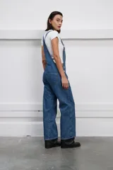 Jardinero denim azul con bolsillo en la pechera, botones metálicos y corte amplio de pierna recta.