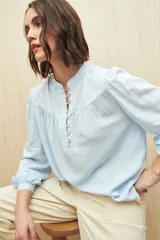Camisa celeste de manga larga en viscosa suave, con cuello mao y botonadura parcial al frente. El detalle de frunces en los hombros y los puños abotonados le suman delicadeza y estilo.