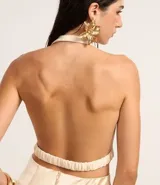 Blusa de crepé color crema, con escote drapeado y espalda descubierta. Presenta aplicaciones de piedras en el frente.