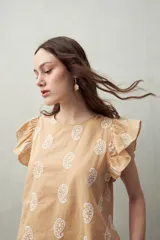 Blusa color beige con estampado paisley blanco, cuello redondo y mangas cortas con volados.